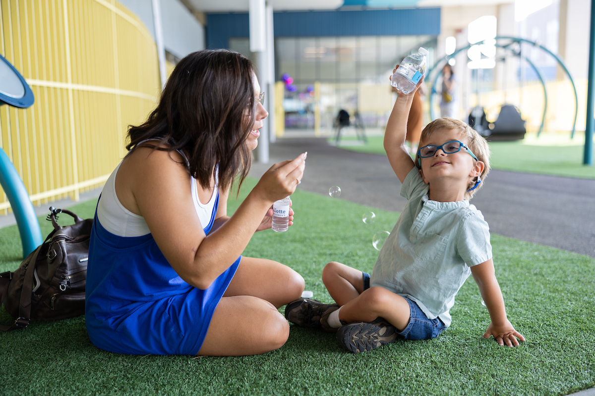 A parent blows bubbles next to her happy child on a playground.