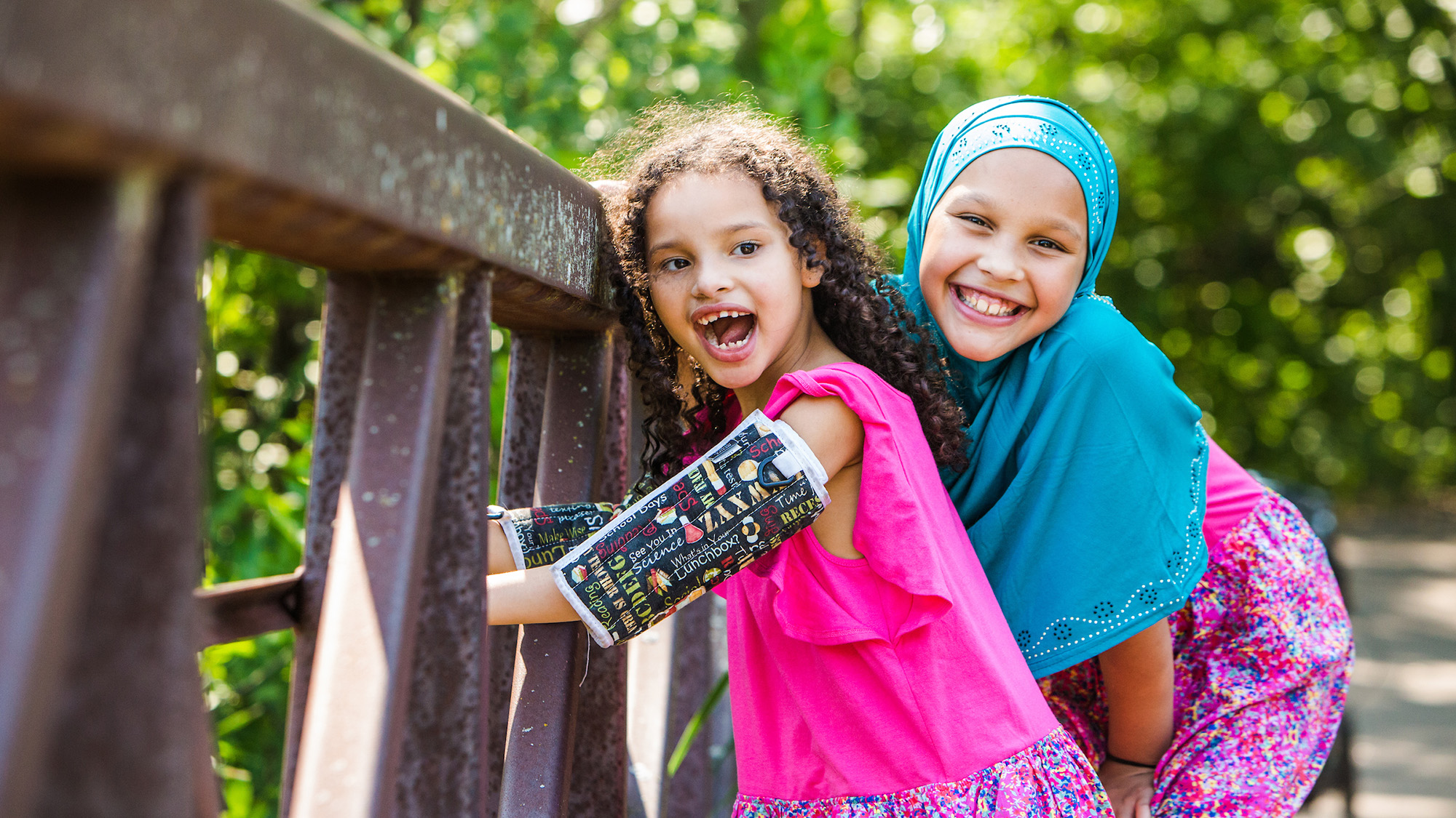 Gillette Children's patient Amatullah Jama smiles along side another girl while standing on a bridge.