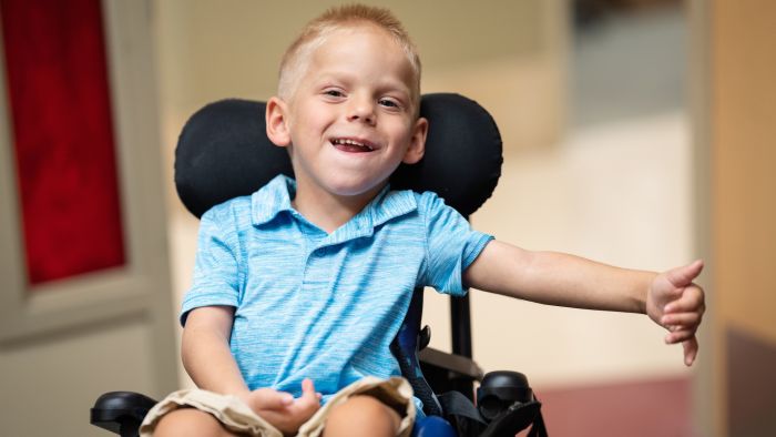 Boy patient at Gillette Children's in a wheelchair giving his care team a thumbs up.