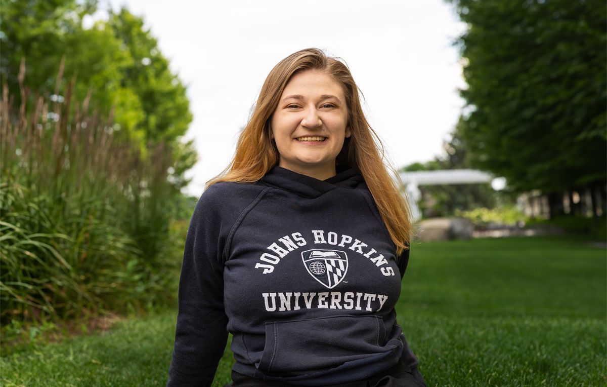 Johns Hopkins pre-med student and Gillette patient, Kate Ketelhohn, sits on the grass at a college campus.