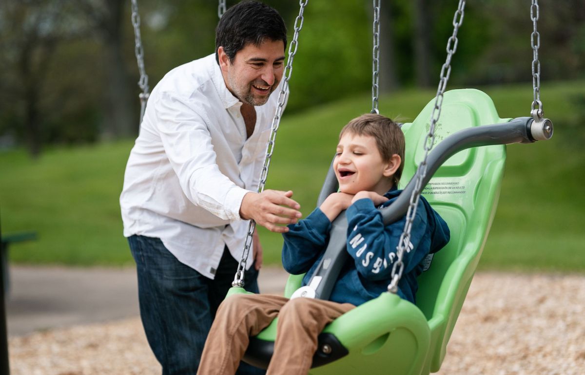 Father pushes his son on a swing designed for children with disabilities.