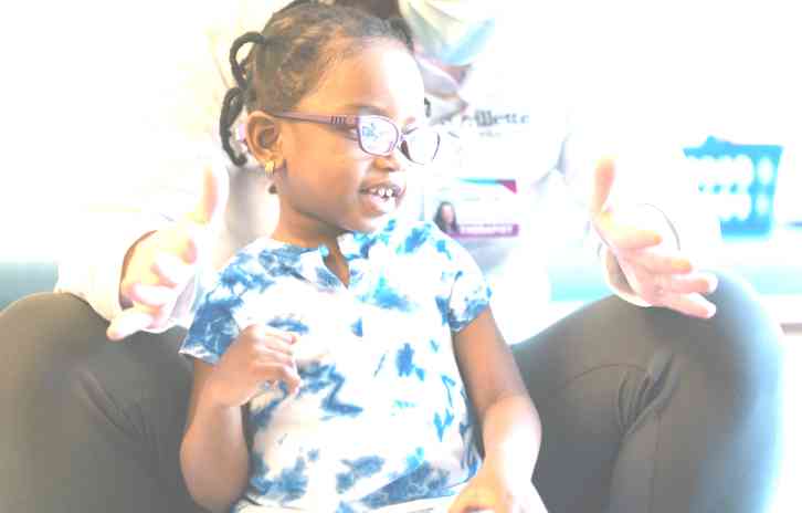 A young African-American girl wearing glasses poses in front of an adult.